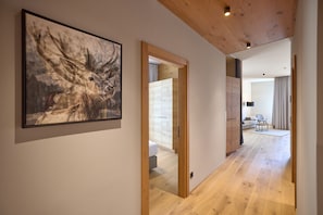 Ein Korridor mit Holzboden, einem gerahmten Kunstwerk an der Wand und einem Blick in einen Wohnbereich mit Sofa und Lampe.