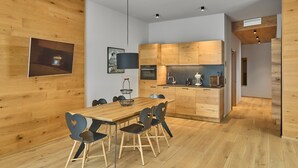 A modern kitchen with wooden cabinets, a dining area with a wooden table and chairs, and a small kitchen island. - 8005 Alpin Retreat Grand 5 (Schröcken)