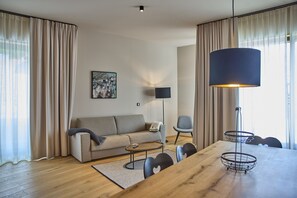 A modern living room with a sofa, a coffee table, a dining table, and a lamp. - 8005 Alpin Retreat Grand 5 (Schröcken)