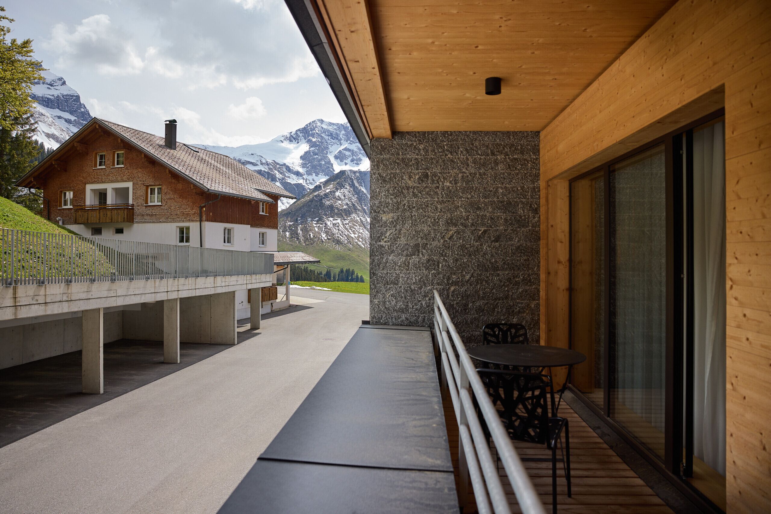 Un balcon offrant une vue sur des montagnes enneigées, un bâtiment en bois et un mur de pierre.