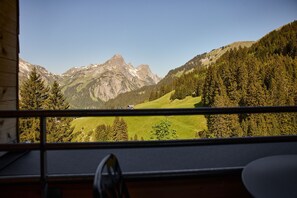 A mountain landscape through a window with a chair and a table visible in the foreground. - 8007 Alpine Retreat 7 (Schröcken)