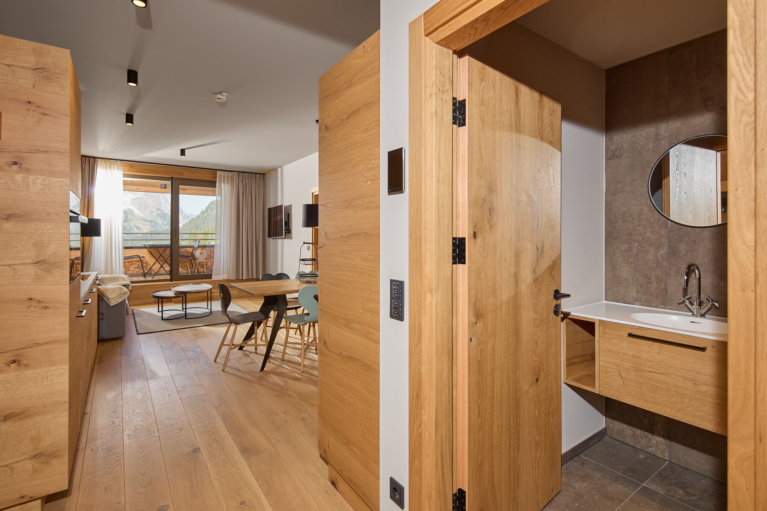 Un intérieur moderne avec un plancher en bois, un coin repas comprenant une table et des chaises, et une salle de bain équipée d’un lavabo et d’un miroir.