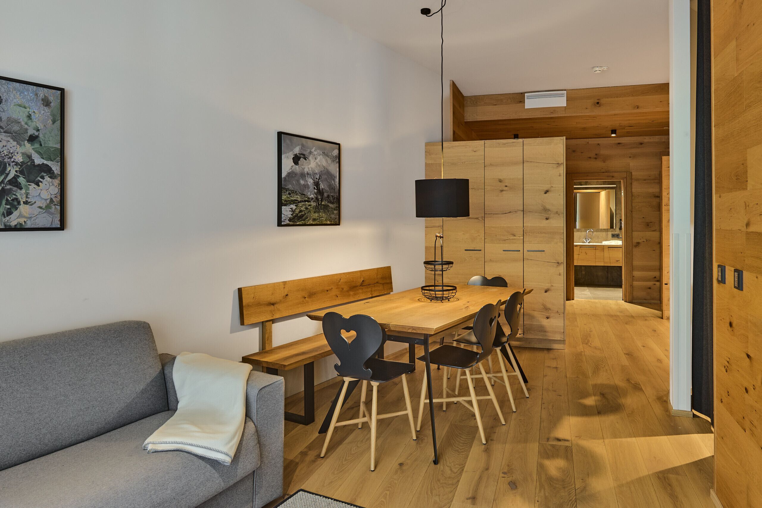 Ein modernes Interieur mit einem Holztisch, Stühlen, einer Bank, einem grauen Sofa und einem großen gerahmten Bild an der Wand.