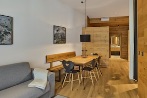 Ein modernes Interieur mit einem Holztisch, Stühlen, einer Bank, einem grauen Sofa und einem großen gerahmten Bild an der Wand.
