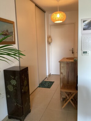 Ein Flur mit einem Holzkasten, einer grünen Matte auf dem Boden, einer Pendelleuchte und einer Tür, an der ein Hut hängt.