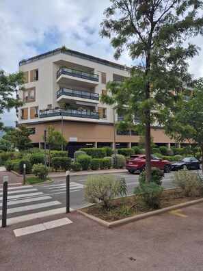 A multi-story residential building with balconies, a parking area, and a pedestrian crossing. - Air-conditioned one-bedroom apartment near the beach with parking and a pool (Le Lavandou)