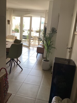 Ein Wohnzimmer mit einer Couch, einem Esstisch und Stühlen. Eine Topfpflanze und ein Fernseher sind ebenfalls vorhanden.