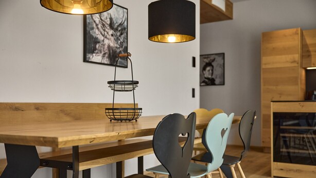 A wooden dining table with chairs, a hanging light fixture, and artwork on the wall. - 8009 Arlberg Grand Residence 9 (Schröcken)
