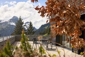 A terrace with a table and chairs, overlooking a mountainous landscape with snow-capped peaks. - 8009 Arlberg Grand Residence 9 (Schröcken)
