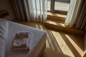 Ein Hotelzimmer mit einem Bett, Holzboden und Blick durch ein Fenster.