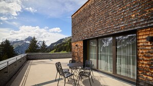 A modern building with a wooden shingle exterior, a balcony with a table and chairs, and a view of mountains. - 8009 Arlberg Grand Residence 9 (Schröcken)