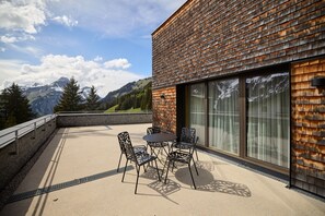 Ein modernes Gebäude mit einer Holzschindel-Fassade, einem Balkon mit Tisch und Stühlen und Blick auf Berge.