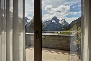 Blick durch ein Fenster auf eine Berglandschaft, einschließlich schneebedeckter Gipfel und einem klaren Himmel.