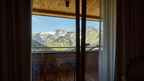 Een houten balkon met twee stoelen en een tafel, met uitzicht op een berglandschap met besneeuwde toppen.