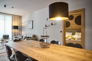 Ein modernes Hotelzimmer mit einem Holztisch, einer Couch, einem Bett mit gelben Handtüchern und einem großen Fenster mit Vorhängen.