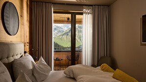 Een hotelkamer met een bed, een stoel, een tafel en uitzicht op bergen door een glazen deur.