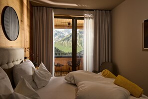 Ein Hotelzimmer mit Bett, Stuhl, Tisch und Blick auf Berge durch eine Glastür.