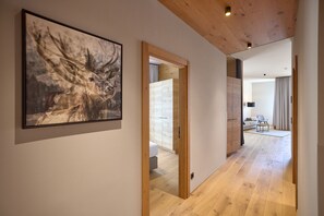 A hallway with wooden flooring, a framed artwork on the wall, and a glimpse of a living area with a sofa and a lamp. - 8012 Alpin Retreat Grand 12 (Schröcken)