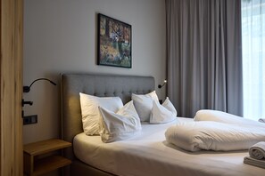 A hotel room with a large bed, a headboard, a painting on the wall, a nightstand, and a window with curtains. - 8012 Alpin Retreat Grand 12 (Schröcken)