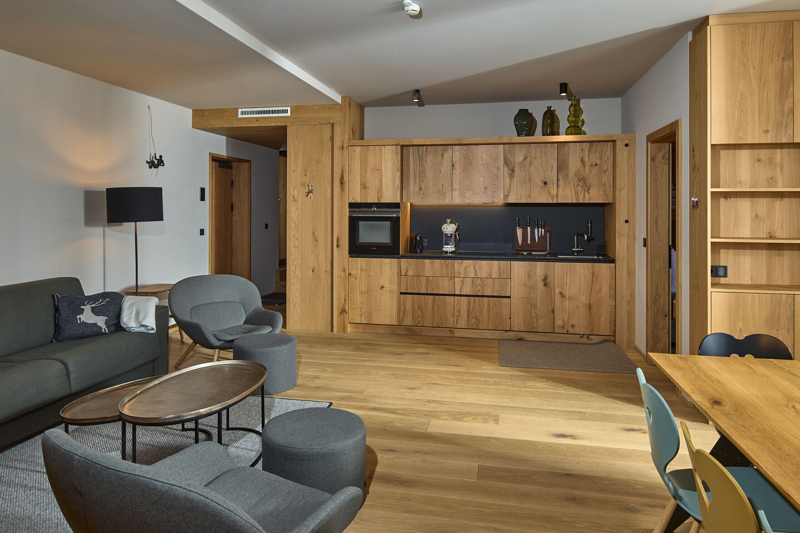 A modern living space with a sofa, armchairs, a coffee table, a dining table, and a kitchen area with wooden cabinets and appliances.