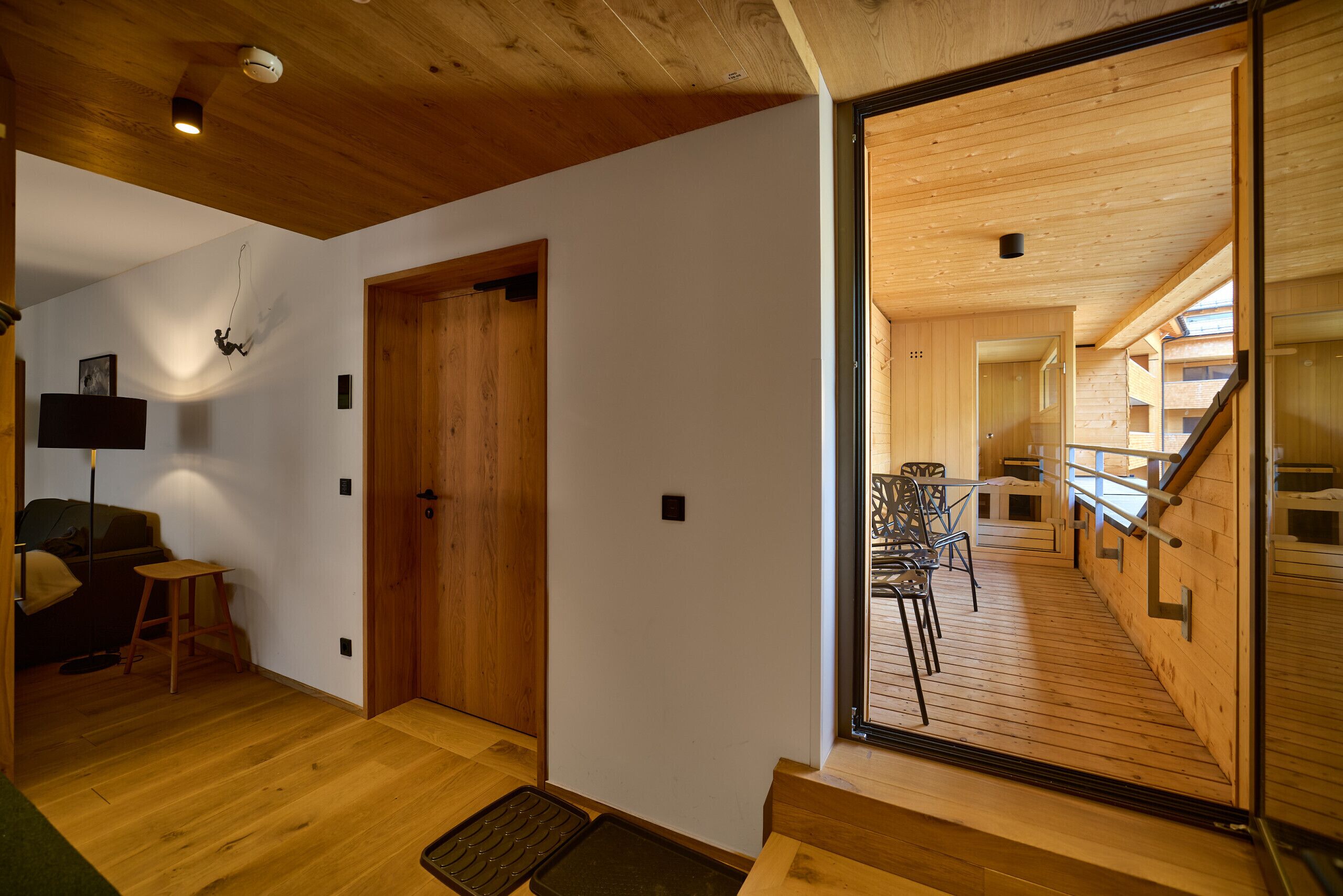 A wooden interior with a staircase leading to an upper level, a seating area with a table and chairs, and a door with a handle.