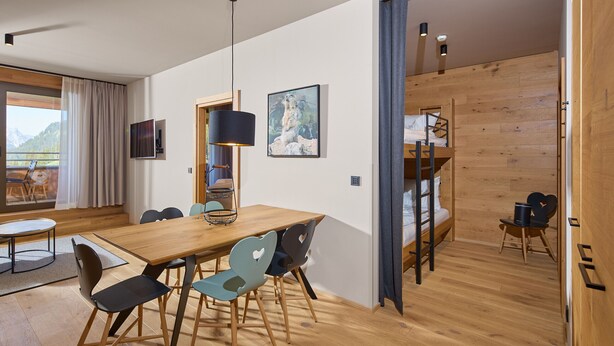 Ein modernes Zimmer mit einem Holzesstisch, Stühlen, einem Fernseher und einem Etagenbett.