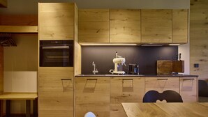 Eine moderne Küche mit Holzschnitzereien, einem Einbauofen, einer Kaffeemaschine und einem Essbereich mit Tisch und Stühlen.