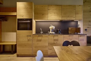 Eine moderne Küche mit Holzschnitzereien, einem Einbauofen, einer Kaffeemaschine und einem Essbereich mit Tisch und Stühlen.