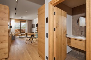 Ein modernes Interieur mit Holzböden, einem Essbereich mit Tisch und Stühlen sowie einem Badezimmer mit Waschbecken und Spiegel.