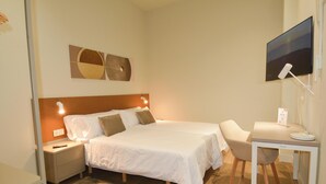A hotel room with a bed, bedside tables, a desk with a chair, a flat-screen TV, and a Wi-Fi sign.