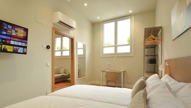 A bedroom with a bed, a desk, a chair, a wardrobe, and a TV mounted on the wall. - GUERNICA Suites Downtown (Gernika-Lumo)