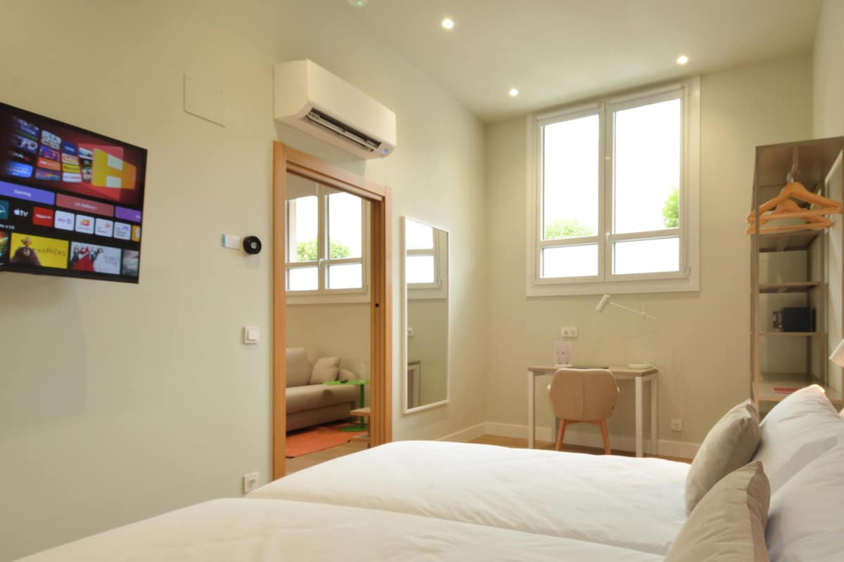 Un dormitorio con cama, escritorio, silla, armario y aire acondicionado.