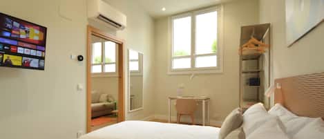 A bedroom with a bed, a desk, a chair, a wardrobe, and a TV mounted on the wall.