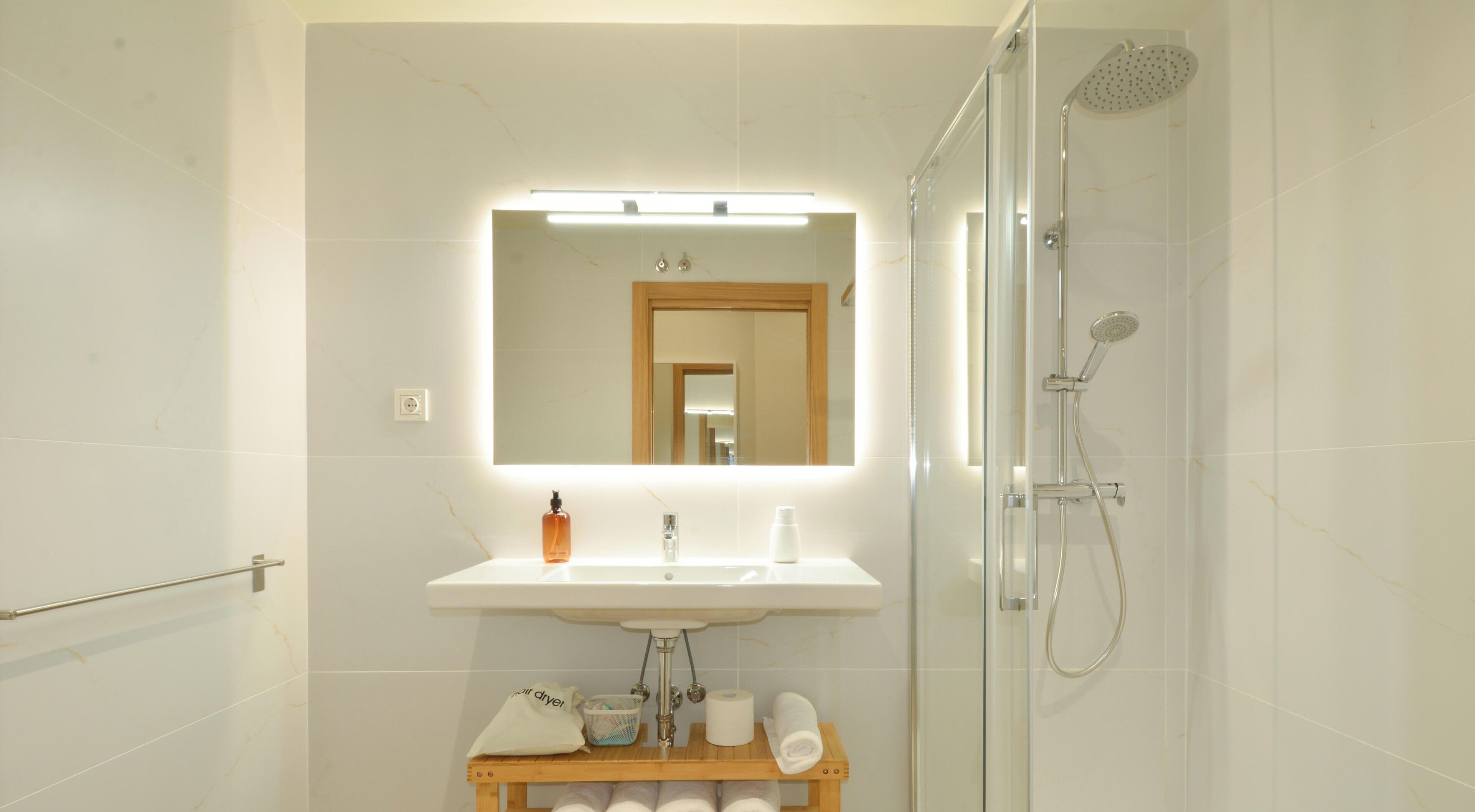 A bathroom with a sink, mirror, shower, and towel rack.