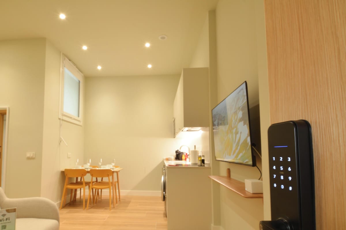 Habitación de hotel con zona de comedor, sofá, televisor y cerradura con teclado.