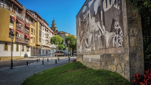 A street with buildings, a mural, and a church in the background. - GUERNICA Suites Downtown (Gernika-Lumo)