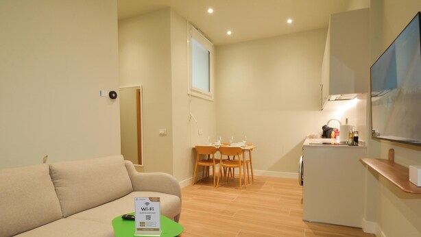 A compact living space with a sofa, a dining table with chairs, a small kitchenette, and a television.