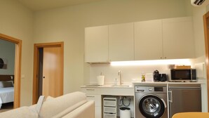 A compact hotel room with a kitchenette, a washing machine, and a bed.