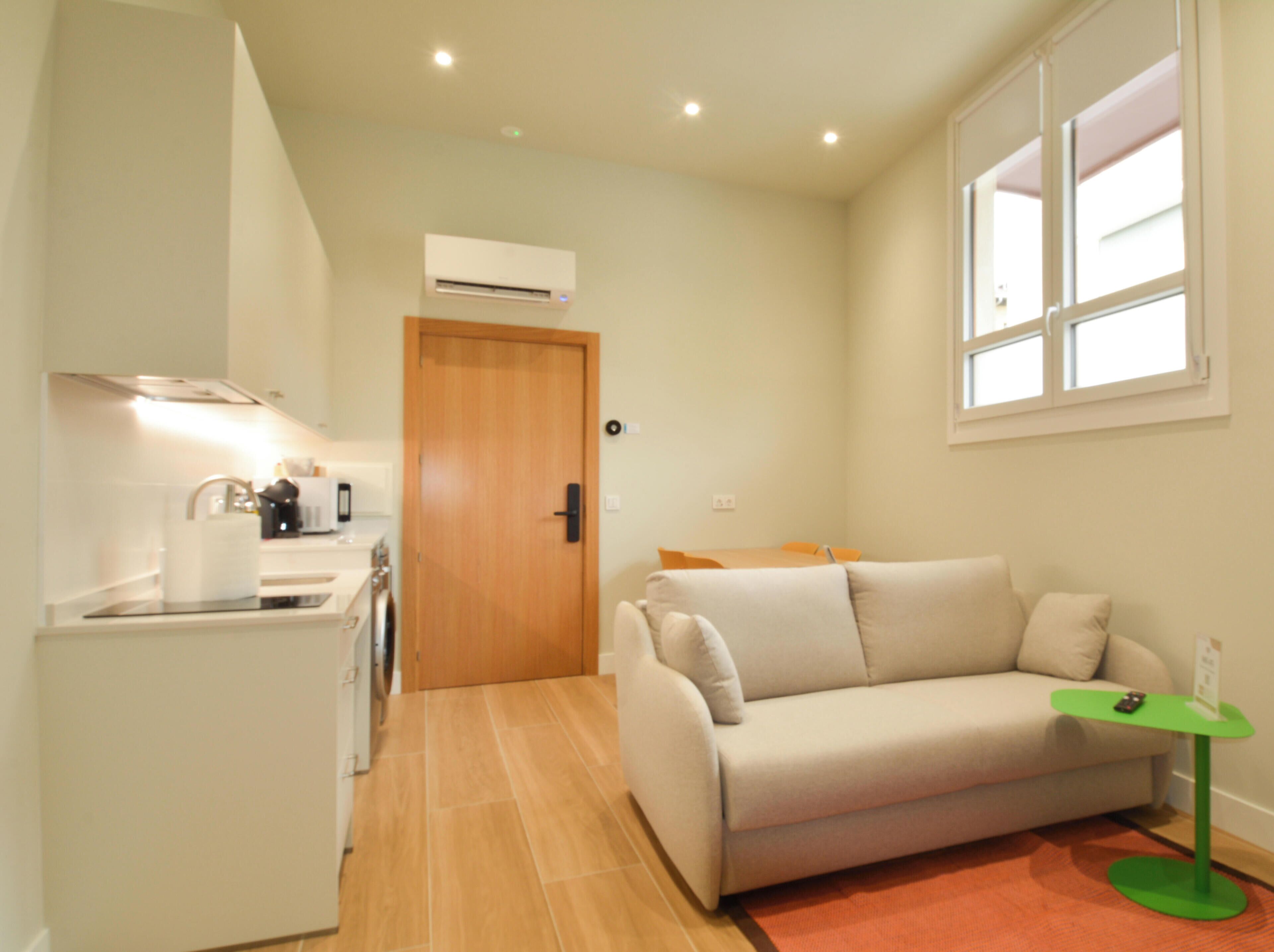 Un espacio habitable compacto con kitchenette, un sofá, una mesita y una ventana.