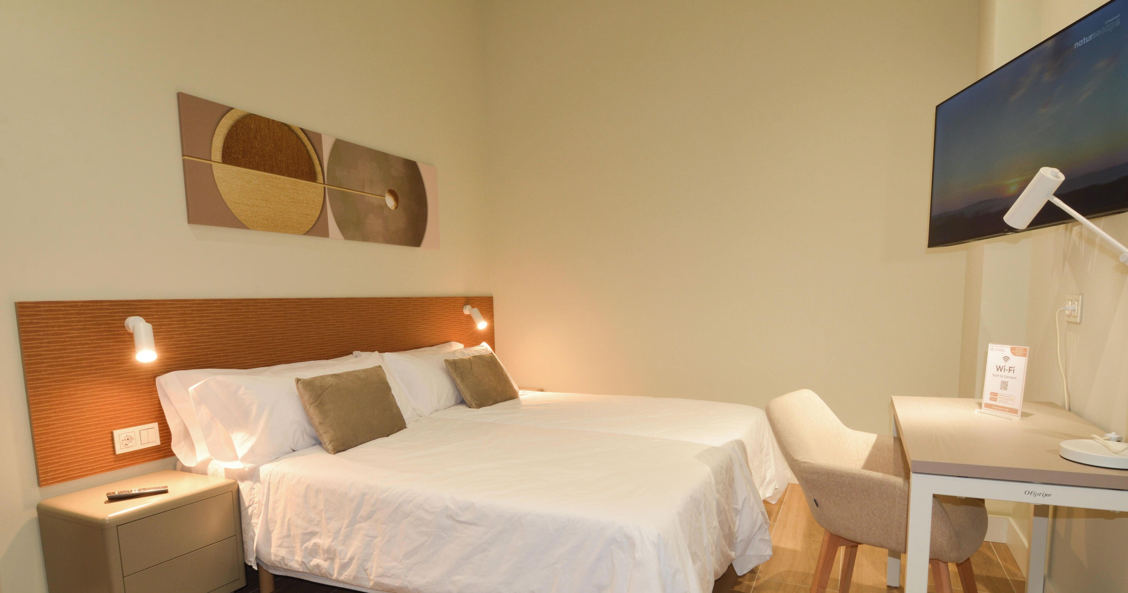 Habitación de hotel con cama, mesitas de noche, escritorio, silla, televisor de pantalla plana y señal de Wi-Fi.
