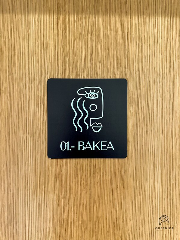 A black sign with a stylized face and the text '01. - BAKEA' on a wooden surface.