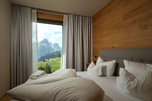 A hotel room with a large bed, wooden headboard, and a view of mountains through sheer curtains. - 8018 Summit Residence 18 (Schröcken)