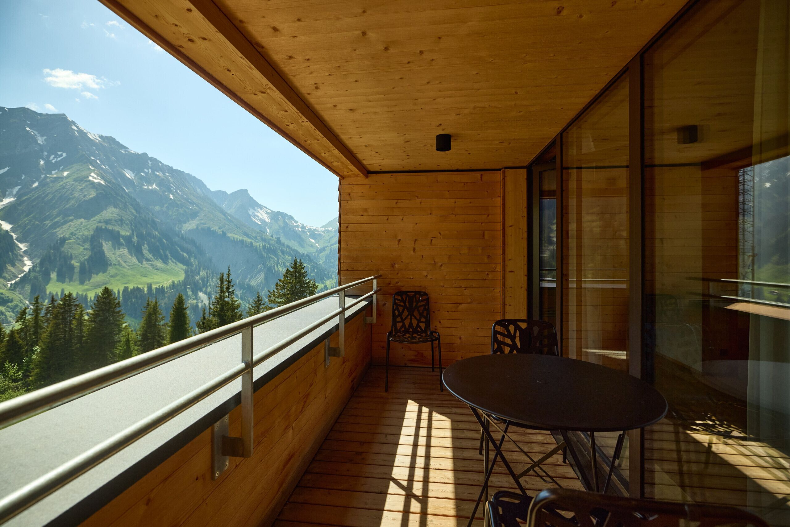 Un balcón de madera con mesa y sillas, con vista a un paisaje montañoso.