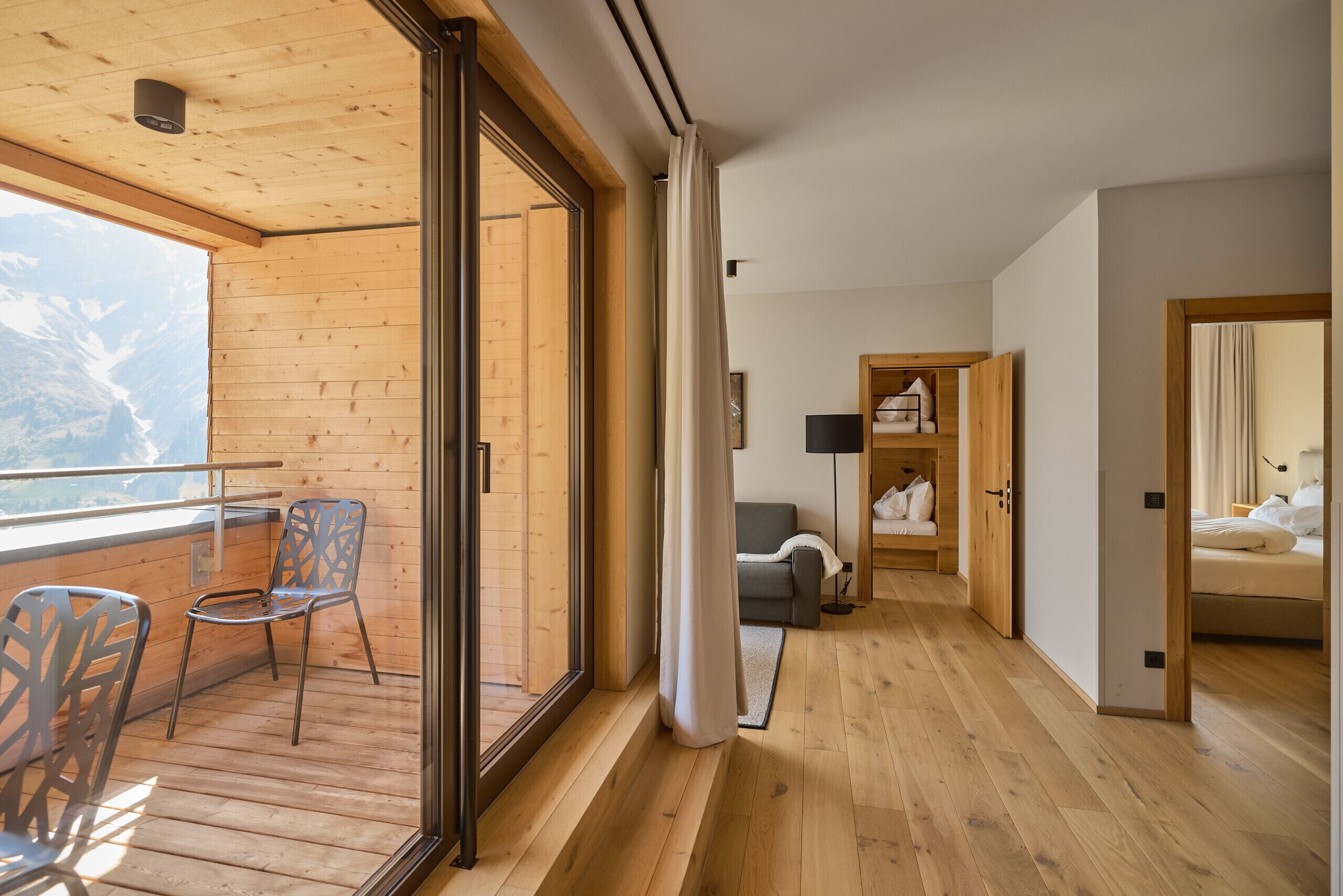 Un interior moderno con piso de madera, un balcón con sillas, un sofá y una cama.