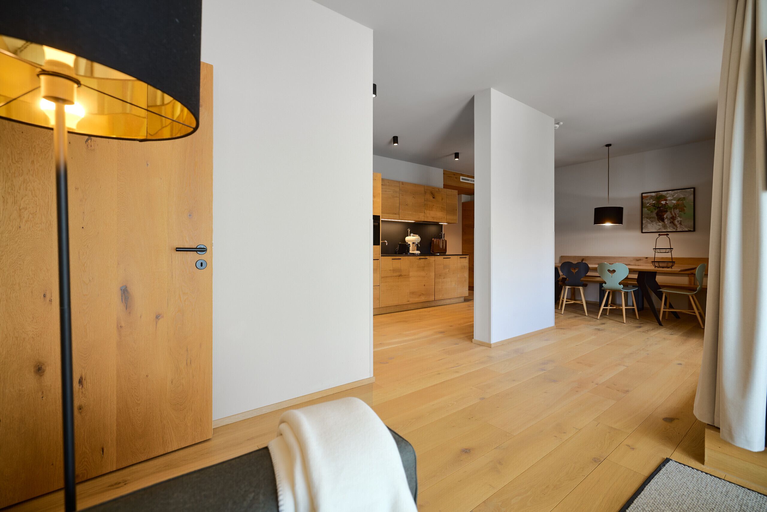 A modern interior with a wooden door, a dining area with chairs, and a kitchen in the background.