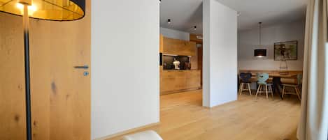 A modern interior with a wooden door, a dining area with chairs, and a kitchen in the background.