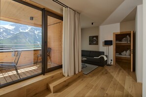 A modern interior with a wooden floor, a balcony with a view of snow-capped mountains, a sofa, and a bed. - 8018 Summit Residence 18 (Schröcken)