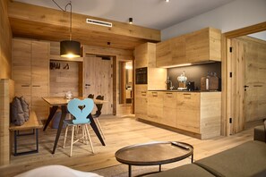 A modern kitchen with wooden cabinetry, a dining area with a heart-shaped chair, and a round coffee table. - 8019 Sky Residence 19 (Schröcken)