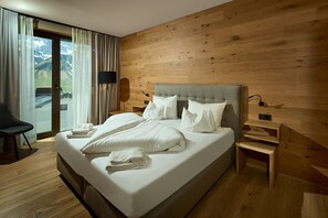 A hotel room with a wooden wall, a bed with white linens, a nightstand, a lamp, and a view of mountains through a window. - 8019 Sky Residence 19 (Schröcken)