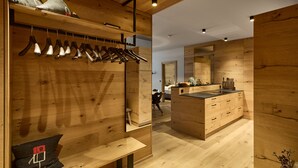 A wooden interior with a clothing rack, a bench, a mirror, and a kitchen area. - 8020 Alpine Residence 20 (Schröcken)